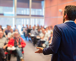 A Your One Degree coach, wearing a blue sportsjacket, discusses the program to a room full of people.